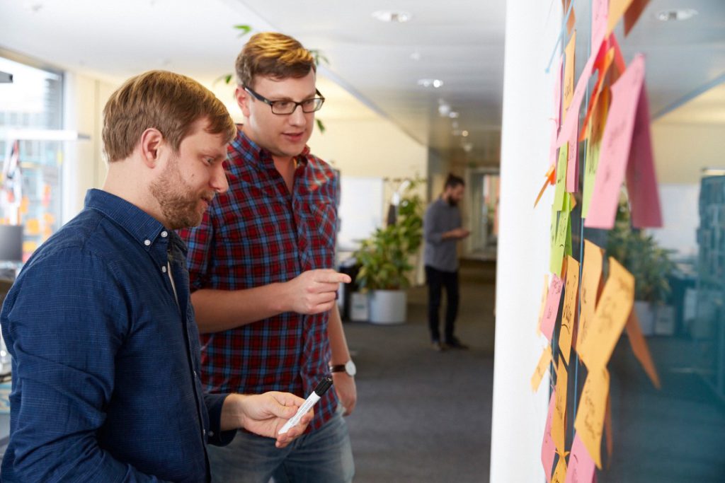 Two men looking at a glass wall with post-its