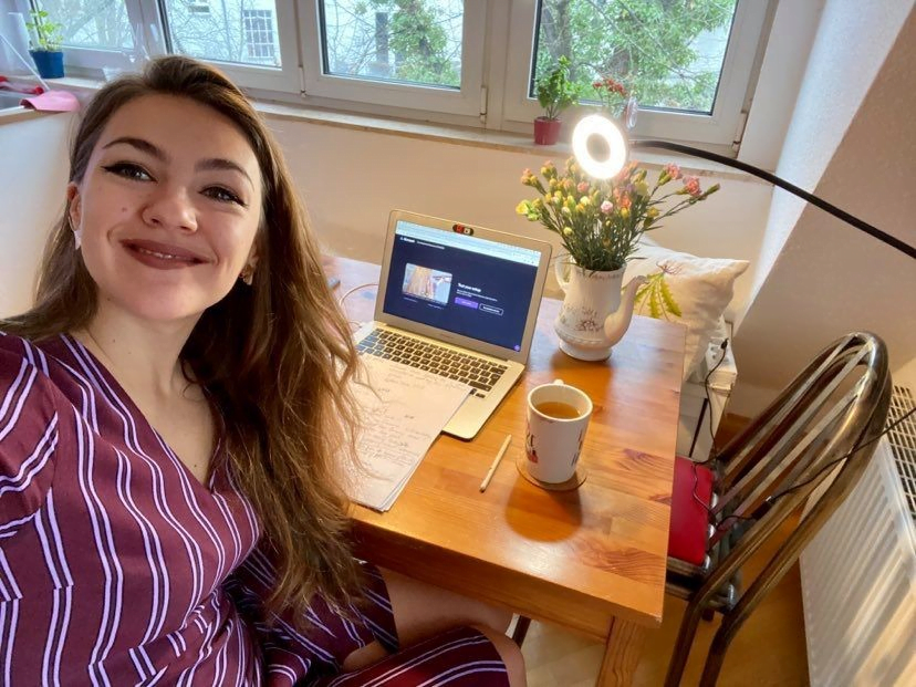 Young woman (Anastasia) taking a selfie sitting on her desk with her laptop, mug and flowers