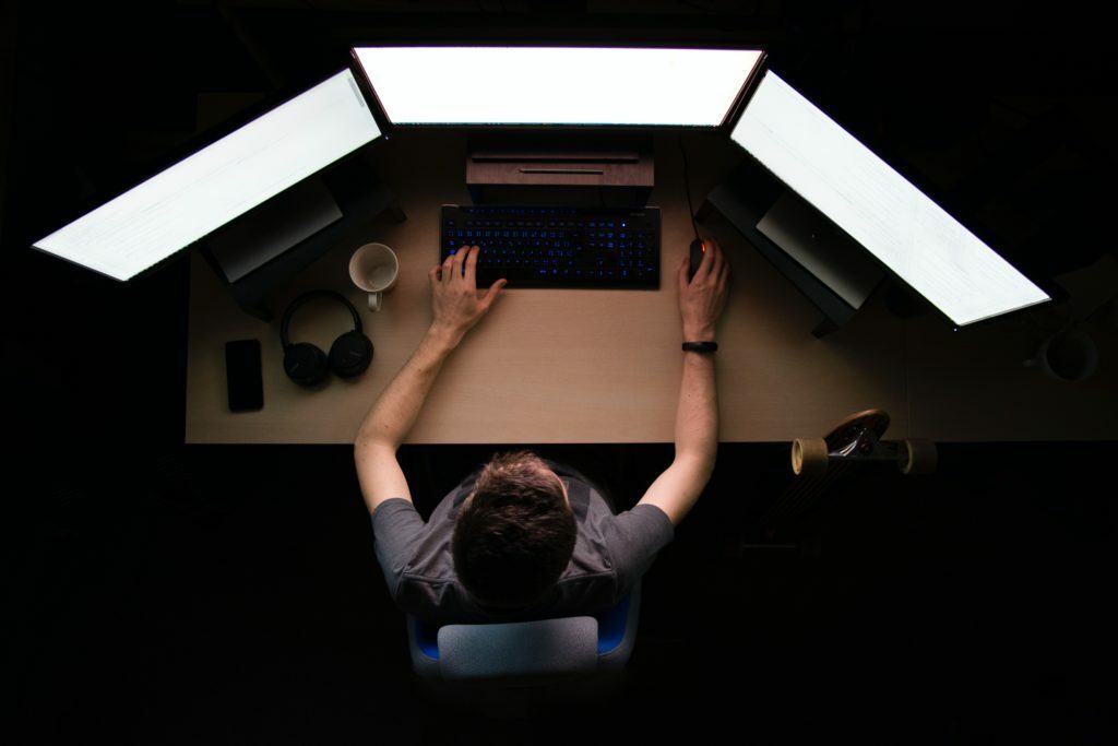 man facing three computer monitors white sitting