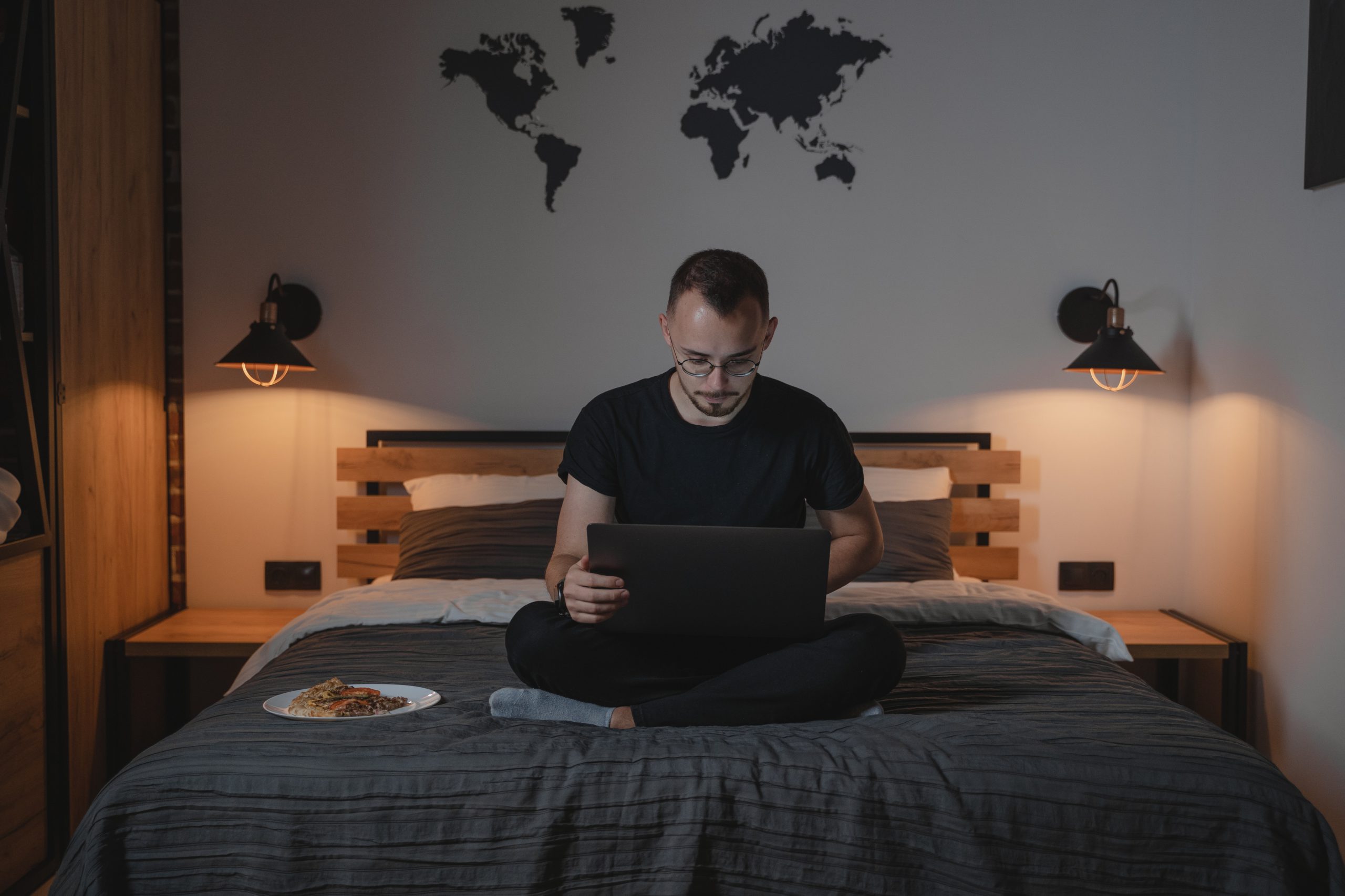 man sitting on his bed working in his computer