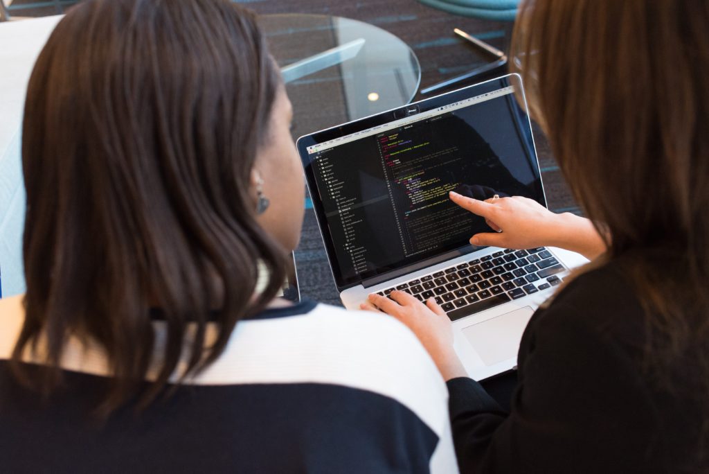 two women looking at code on a macbook
